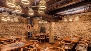 A rustic dining area with wooden tables and chairs, stone walls, and hanging pendant lights. - Goldener Engl (Hall In Tirol)