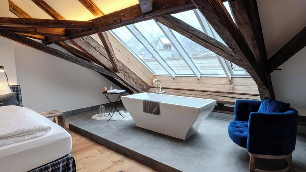 A modern bathroom with a freestanding bathtub, a blue chair, and a skylight. - Goldener Engl (Hall In Tirol)