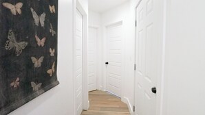 Ein Flur mit weißen Wänden, Holzboden und einer Wandteppich mit Schmetterlingsmotiv. Auf beiden Seiten befinden sich weiße Türen.