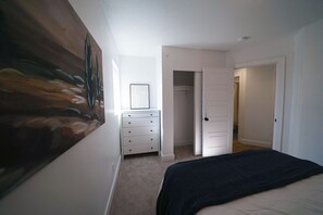 Une chambre à coucher avec un lit, une commode, un tableau et un placard.