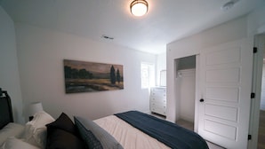 Ein Schlafzimmer mit Bett, Kissen, einem Gemälde, einer Kommode und einer Tür.
