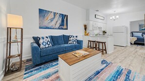 Een moderne woonkamer met een blauwe bank, een houten salontafel en een kleurrijk vloerkleed.