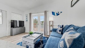 Un salon avec un canapé bleu, une table basse, un téléviseur à écran plat et une porte-fenêtre coulissante donnant sur un espace extérieur.