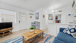A modern living room with a television, a wooden coffee table, a blue sofa, and a kitchen area with cabinets and a countertop. - Waterfront Modern Condo | Pet Friendly near Beach! (Indian Rocks Beach)