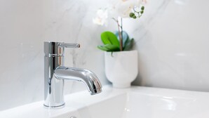 Une salle de bain moderne avec un robinet chromé, des murs en marbre blanc et une orchidée en pot.