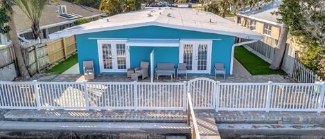 Una casa de dos pisos con fachada azul, un patio trasero cercado y una terraza con muebles de exterior.