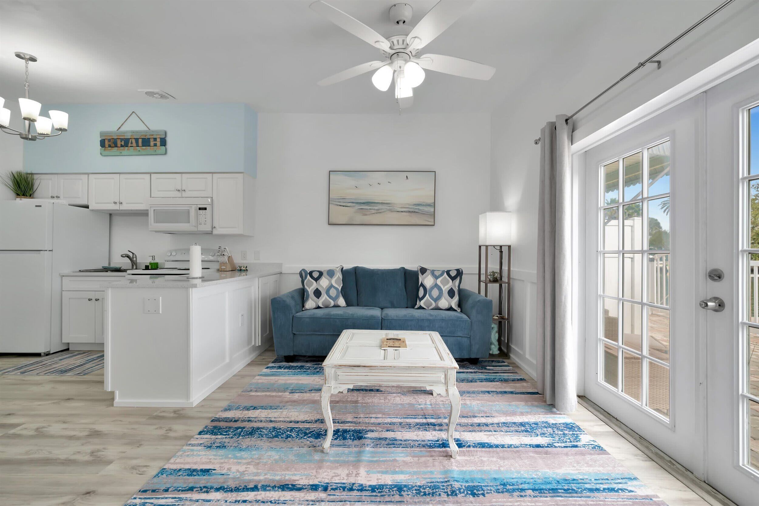A modern living room with a white coffee table, a blue sofa with patterned cushions, and a painting on the wall.