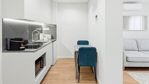 A compact kitchen with modern appliances, a dining area with a blue chair, and a grey sofa in a bright, minimalist room. - GuestReady The 7 Seas - Caspian Sea 1E (Porto)