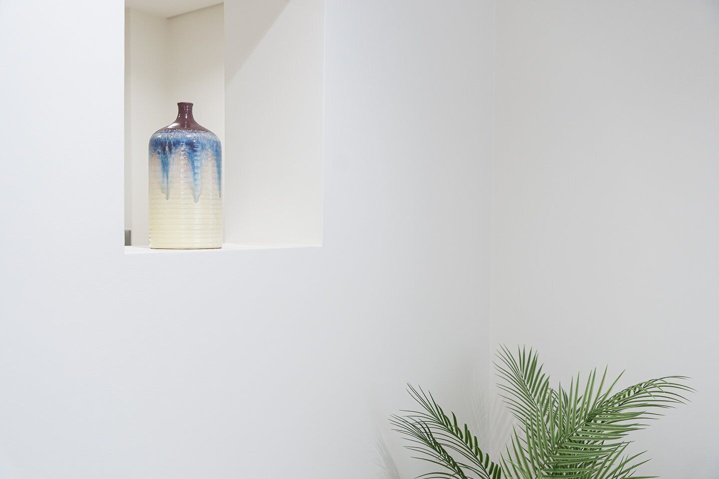 A white wall with a window revealing a blue and white vase.