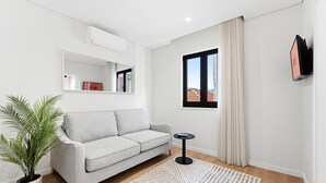 A modern living room with a grey sofa, a small round table, a potted plant, and a large window with curtains. - GuestReady The 7 Seas - Caspian Sea 1E (Porto)