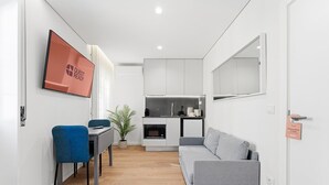 A compact living space with a kitchenette, a sofa, a dining area with a table and chairs, and a TV mounted on the wall. - GuestReady The 7 Seas - 'Caribbean Sea' 1D (Porto)
