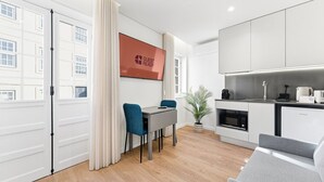 A modern hotel room with a dining area, kitchenette, and a large window with curtains. - GuestReady The 7 Seas - 'Caribbean Sea' 1D (Porto)