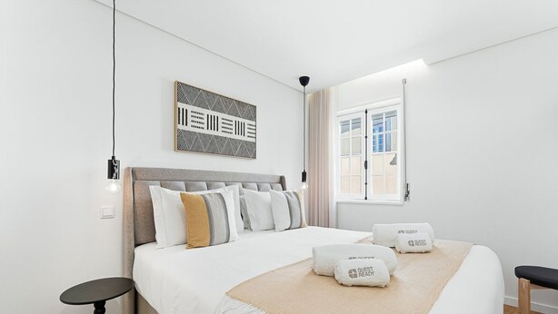 A modern hotel room with a large bed, a headboard, a bedside table, a window, and a wall-mounted artwork. - GuestReady The 7 Seas - 'Caribbean Sea' 1D (Porto)