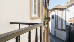 A narrow street with buildings on either side, a balcony with a metal railing, and a window with a white frame. - GuestReady The 7 Seas - 'Caribbean Sea' 1D (Porto)