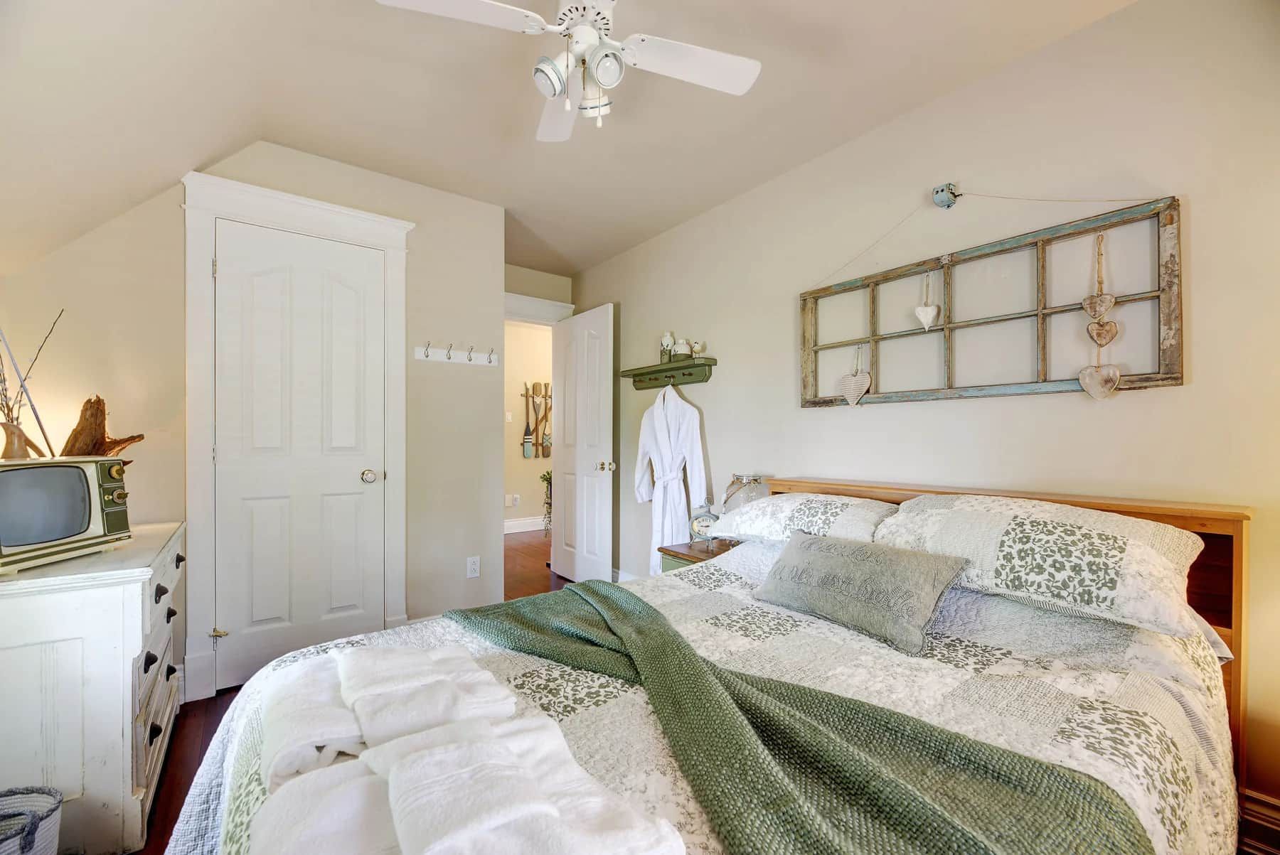 A bedroom with a bed, a white dresser, a television, and a ceiling fan.