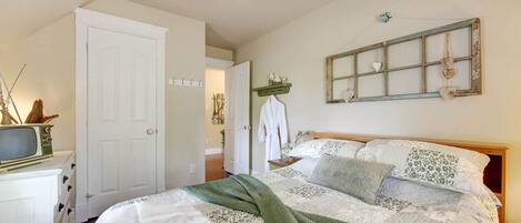 A bedroom with a bed, a white dresser, a television, and a ceiling fan.