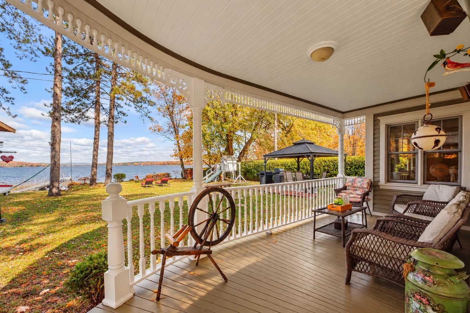 A covered porch with a view of a lake, a swing set, and outdoor seating.