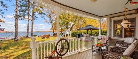 A covered porch with a view of a lake, a swing set, and outdoor seating.