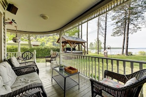 A covered porch with wicker furniture, a small gazebo, and a view of a lake.