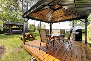 A covered outdoor patio with a table and chairs, a grill, and a hot tub.