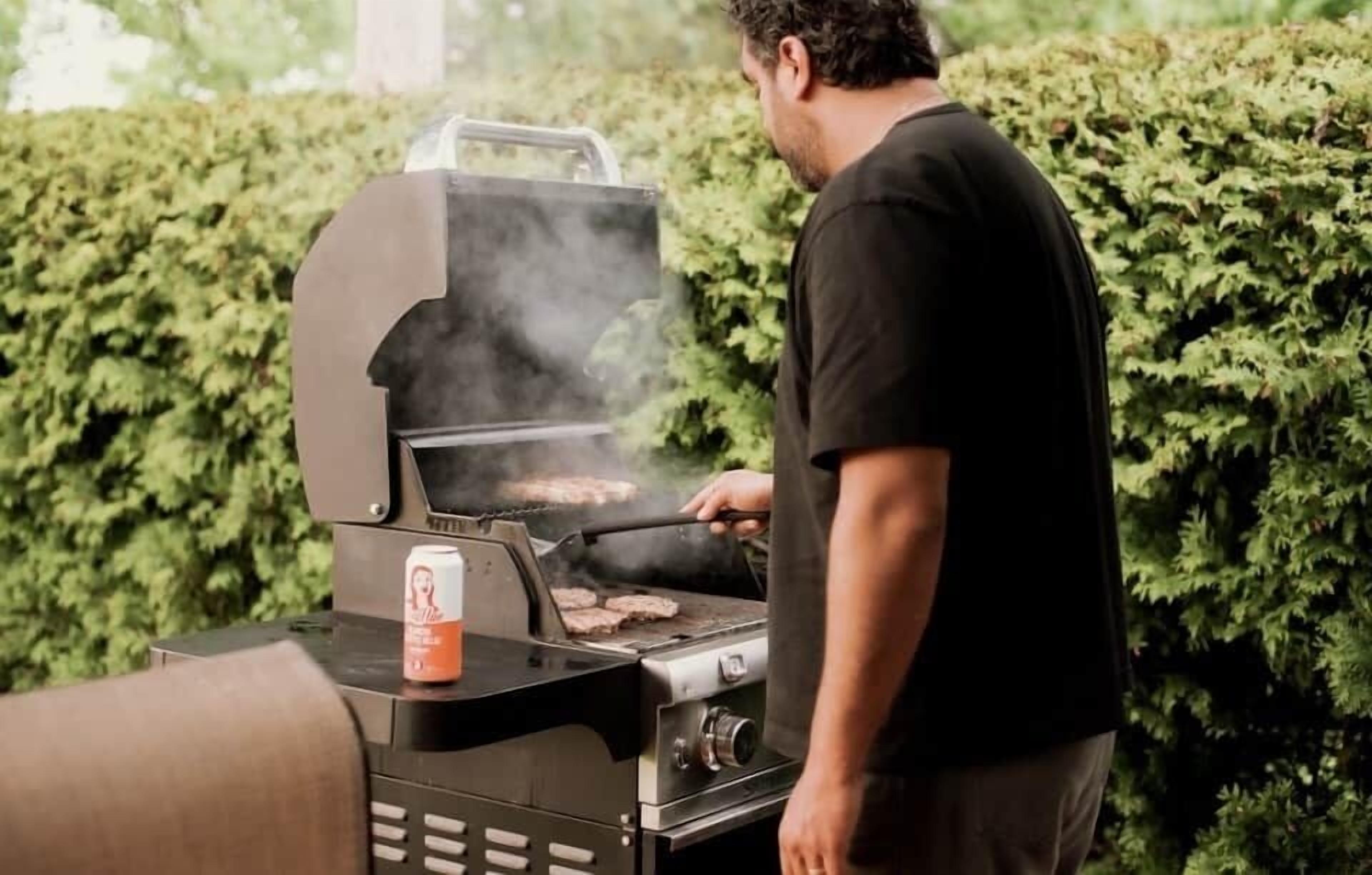 Alguém assando ao ar livre com uma lata de cerveja na churrasqueira.