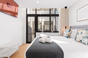 A modern hotel room with a large bed, a view of the city through a window, a white radiator, and a framed picture on the wall. - GuestReady The 7 Seas - Red Sea Groundfloor (Porto)