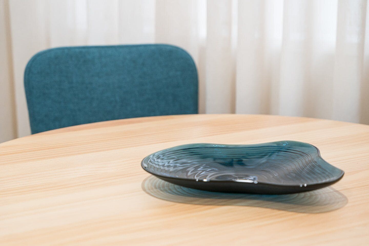 Une table ronde en bois sur laquelle repose un objet en verre foncé, à la texture particulière.
