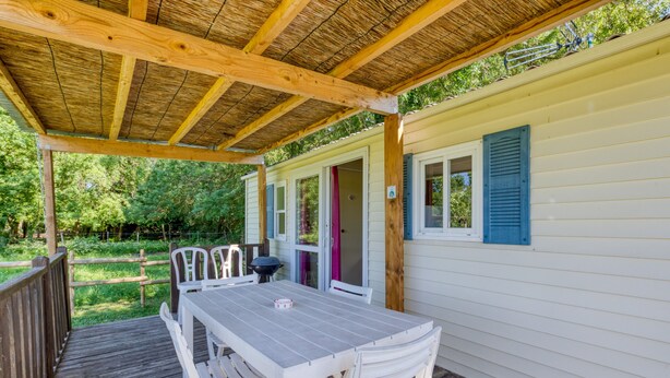 A covered patio with a table and chairs, a wooden deck, and a small building with a door and windows.