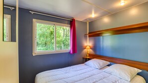 A bedroom with a bed, a window with curtains, a nightstand with a lamp, and a headboard.