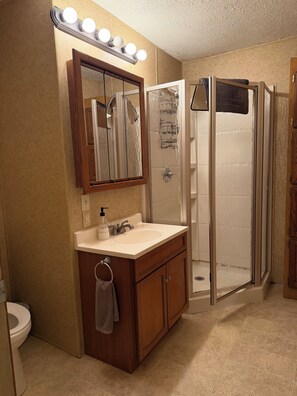 A bathroom with a vanity, sink, mirror, and a walk-in shower. - Crossover Cabin is ready for your outdoor adventure! Perfect for snowmobilers!! (Munising)