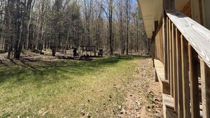 A wooden deck with a view of a forested area and a picnic table. - Crossover Cabin is ready for your outdoor adventure! Perfect for snowmobilers!! (Munising)
