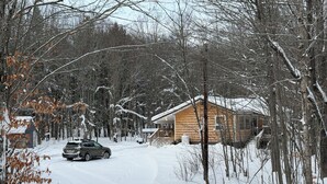 A cabin with a wooden exterior, a snow-covered driveway, and a car parked in front. - Crossover Cabin is ready for your outdoor adventure! Perfect for snowmobilers!! (Munising)