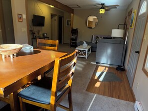 A dining area with a wooden table and chairs, a television mounted on the wall, and a ceiling fan. - Crossover Cabin is ready for your outdoor adventure! Perfect for snowmobilers!! (Munising)