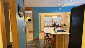 A modern kitchen with a central island, wooden stools, a sink, and a refrigerator. - Crossover Cabin is ready for your outdoor adventure! Perfect for snowmobilers!! (Munising)