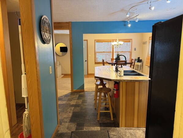 Eine moderne Küche mit einer zentralen Kochinsel, Holzstühlen, einer Spüle und einem Kühlschrank.
