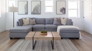 Ein modernes Wohnzimmer mit einem grauen Ecksofa, einem Holztisch und einem gemusterten Teppich.