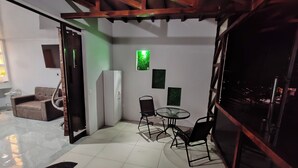 A small, well-lit room with a sofa, a glass table, and chairs. There is a door leading to another room, and a window with a view of the outside. - Modern Aparm with Private Jacuzzi •Arenal Volcano View • 3 Minutes from Downtown (La Fortuna)