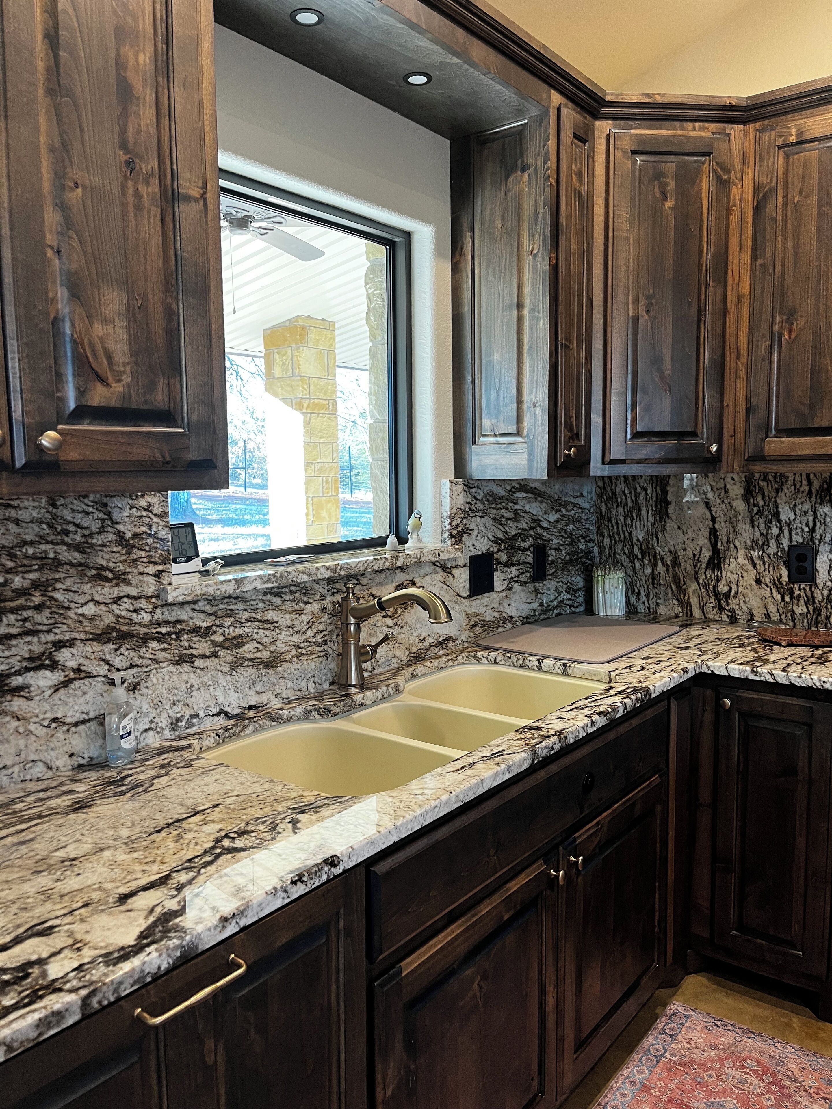 A kitchen with dark wooden cabinets, a granite countertop, and a window with a view of a stone building.