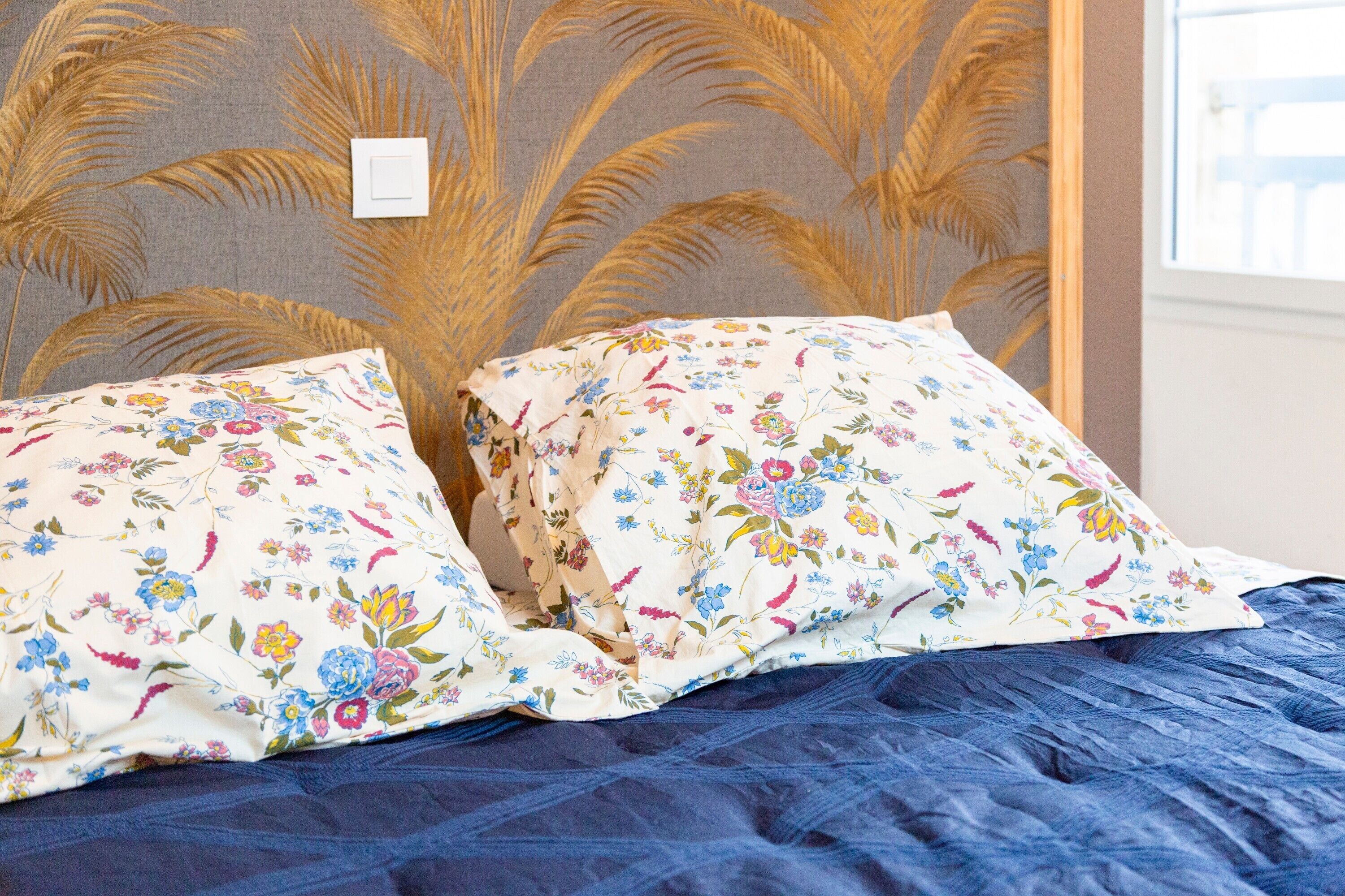 Un lit avec des oreillers à motifs floraux et une couverture bleue.