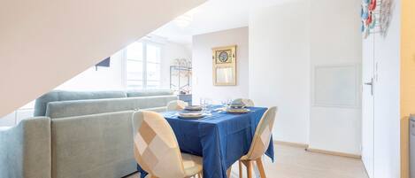 Un coin repas avec une table dressée pour quatre personnes, un canapé et une fenêtre avec des stores.