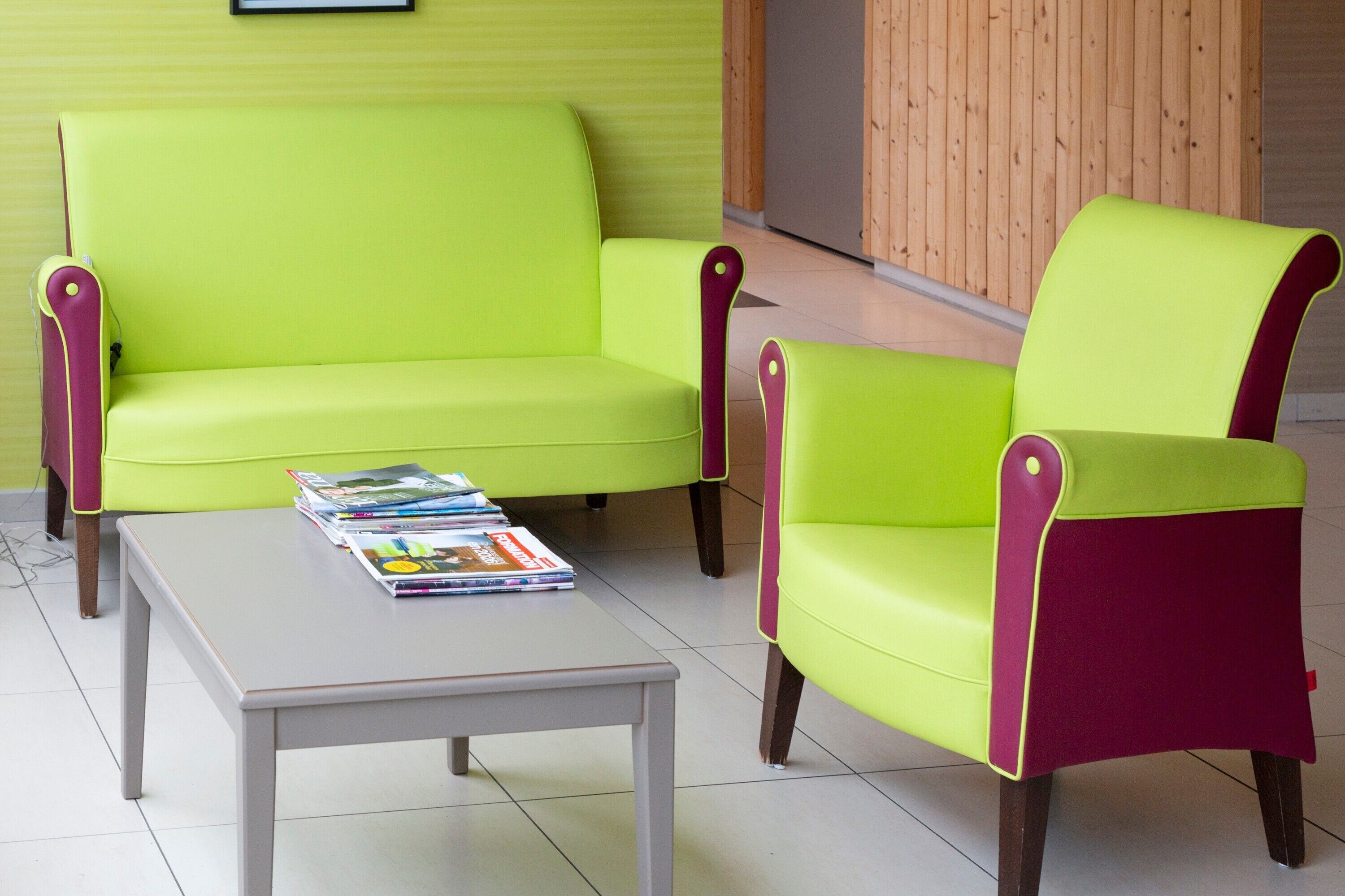 Una habitación luminosa con un sofá verde, un sillón a juego y una pequeña mesa blanca con revistas.