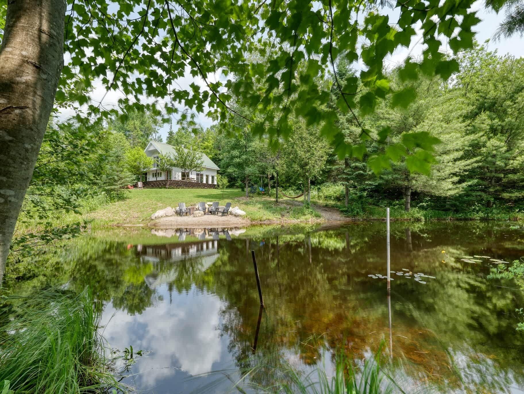 Une maison située près d’un étang, avec une terrasse et des chaises.