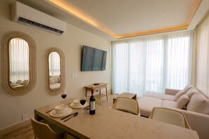 A hotel room with a dining area, a sofa, a TV, and large windows with sheer curtains. - New front beach apartment with golf cart (Puerto Morelos)
