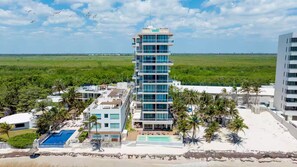 A multi-story hotel with a pool, beach view, and palm trees. - New front beach apartment with golf cart (Puerto Morelos)