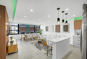 Un intérieur moderne comprenant un coin repas, des canapés blancs, un îlot de cuisine et des luminaires suspendus.