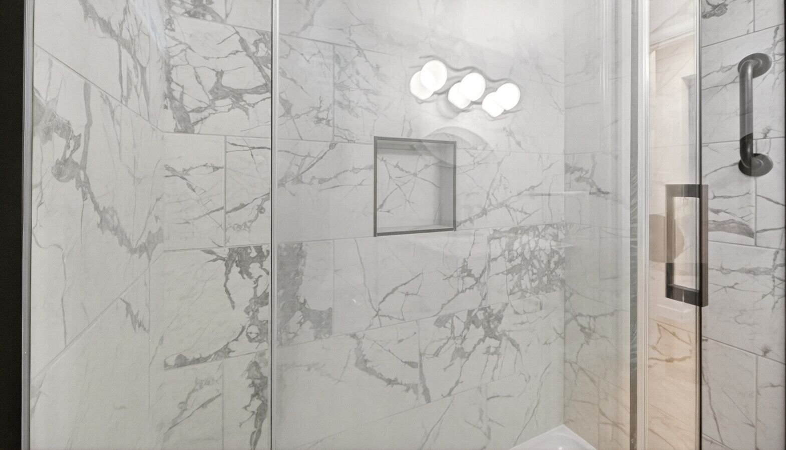 A modern bathroom with marble walls, a glass shower enclosure, and a visible handrail.