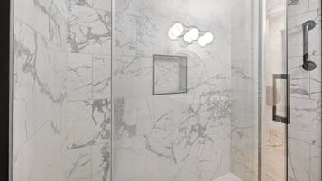 A modern bathroom with marble walls, a glass shower enclosure, and a visible handrail.