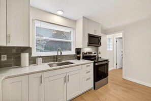 A modern kitchen with white cabinets, a stainless steel sink, a microwave, and an oven. - Quiet Modern 2BR w/ Patio & Garage in North Canton (North Canton)