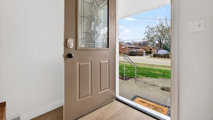 Puerta color beige con panel de vidrio y cerradura electrónica, que da a un porche cubierto con felpudo.