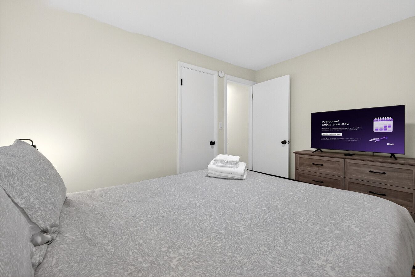 A hotel room with a bed, a TV, a wardrobe, and a set of doors.